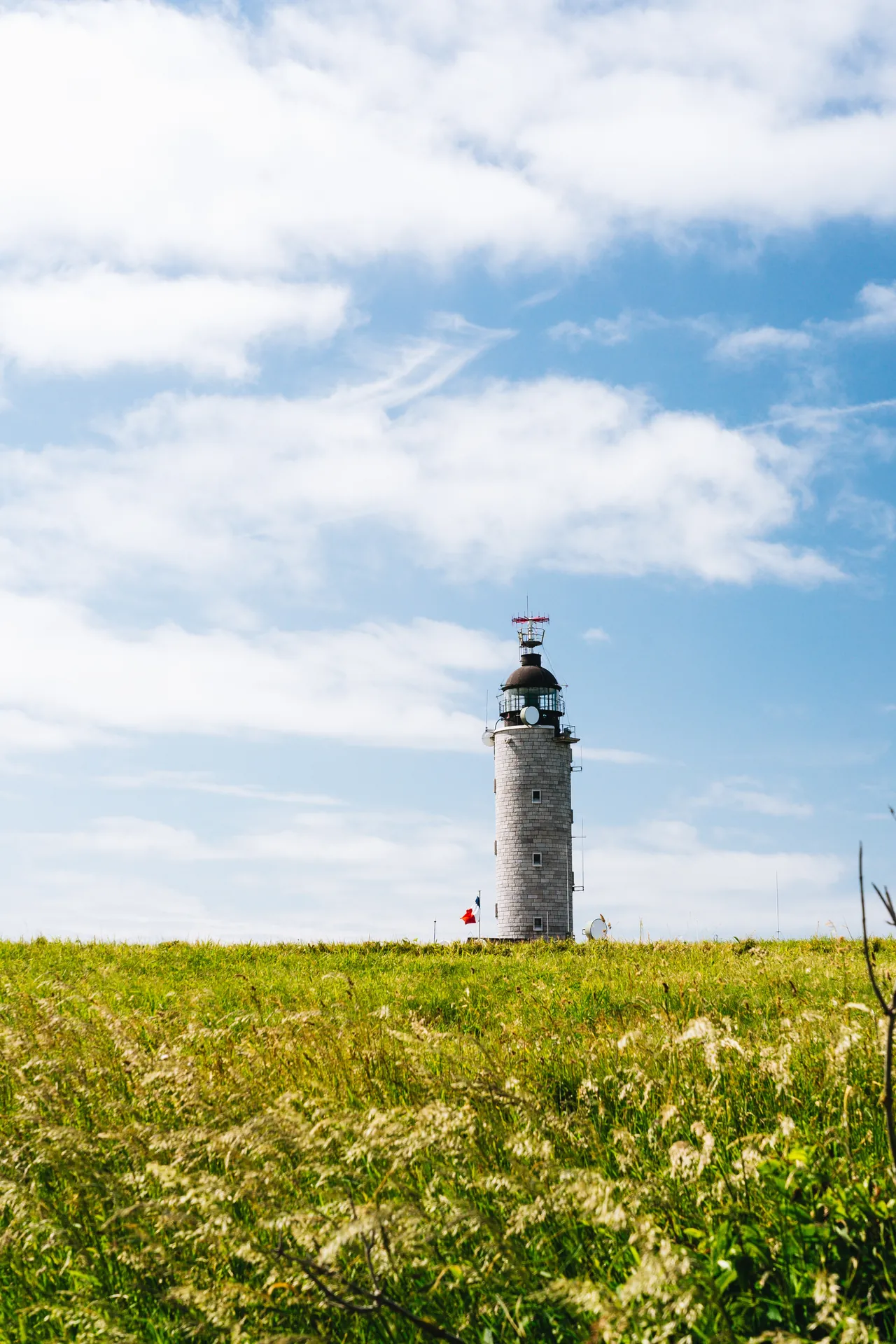 Champ de verdure face à un phare au loin, sous un ciel doux